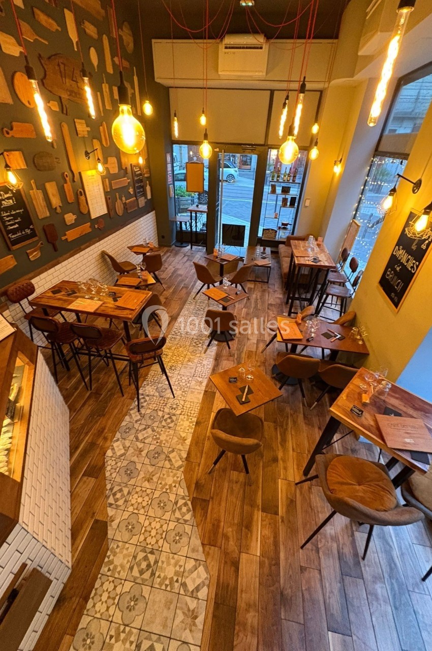 Salle de restaurant chaleureuse avec tables en bois, éclairage suspendu et décoration murale variée.