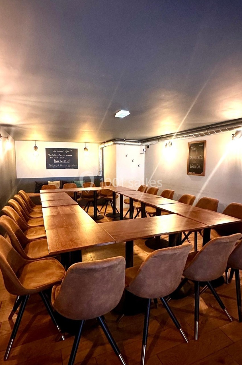Salle de réunion avec une grande table en U entourée de chaises en cuir, éclairée par des appliques murales.