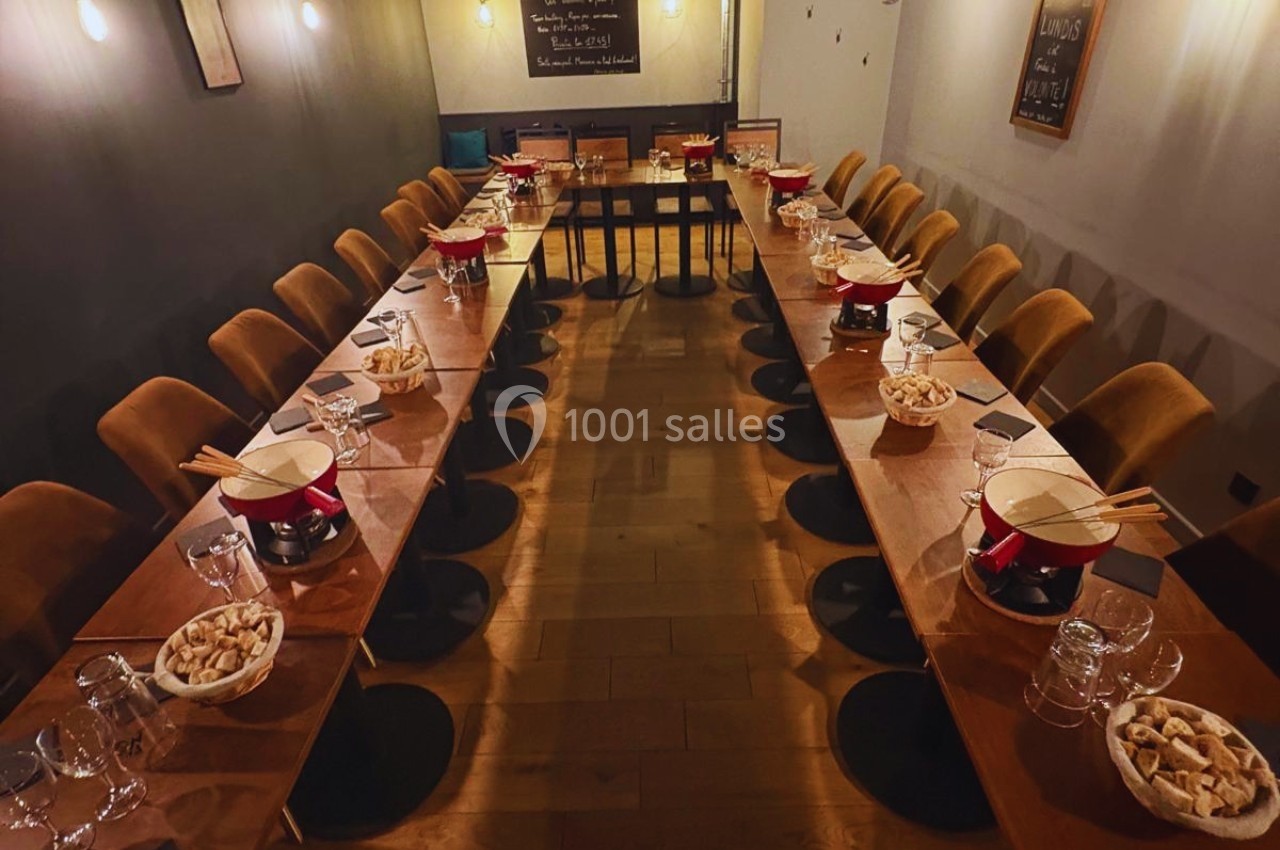 Salle de restaurant avec deux longues tables dressées pour un repas, comprenant des caquelons à fondue et des…