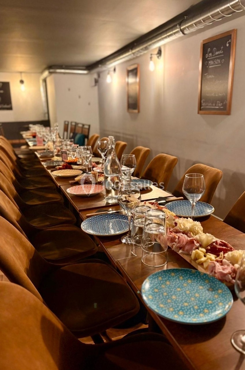 Grande table en bois dressée pour un repas, avec assiettes colorées, verres, carafes et plateaux de charcuterie.