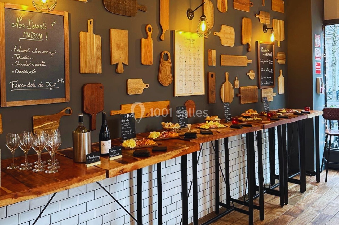 Salle décorée de planches en bois avec un buffet de fromages, vins et desserts disposé sur des tables en bois.