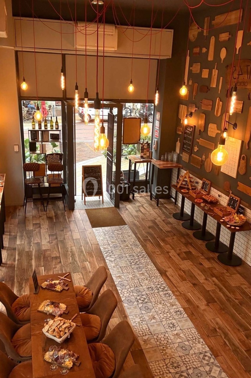 Intérieur d'un café chaleureux avec éclairage suspendu, tables en bois, sol en carreaux et vue sur l'extérieur.