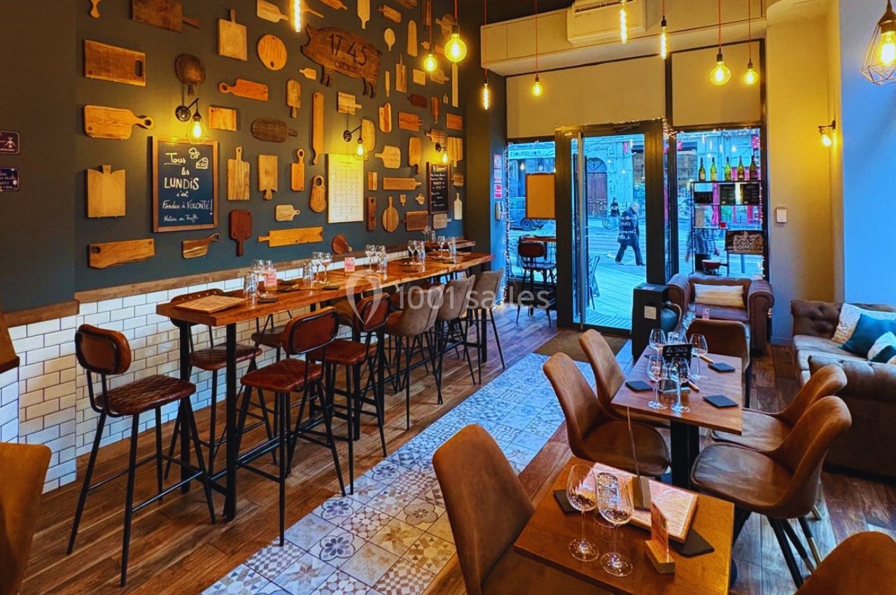 Salle de restaurant chaleureuse avec tables en bois, chaises hautes, murs décorés de planches et éclairage suspendu.