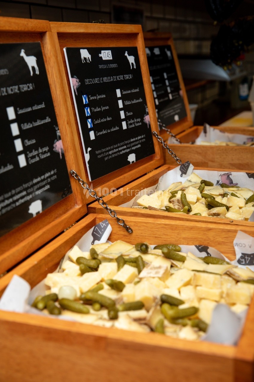 Plateaux en bois contenant des morceaux de fromage et des cornichons, présentés devant des panneaux explicatifs.