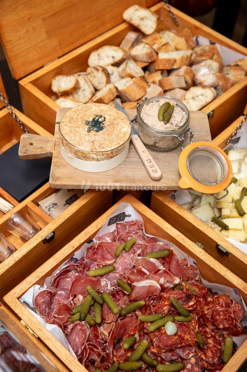 Plateau de charcuterie avec cornichons, fromage, pain et rillettes présentés dans des boîtes en bois ouvertes.