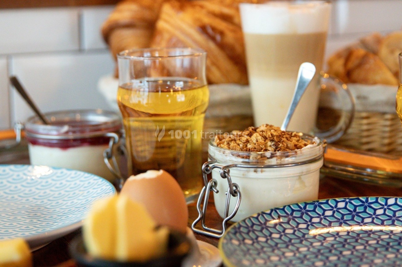 Petit-déjeuner avec yaourt au granola, jus, café, croissants et beurre sur une table en bois.