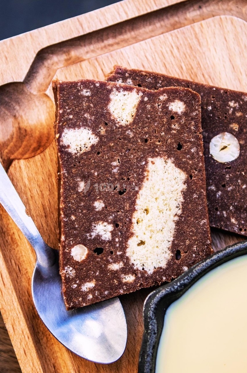 Deux tranches de gâteau marbré au chocolat et à la vanille sur une planche en bois, avec une cuillère et un bol de crème.