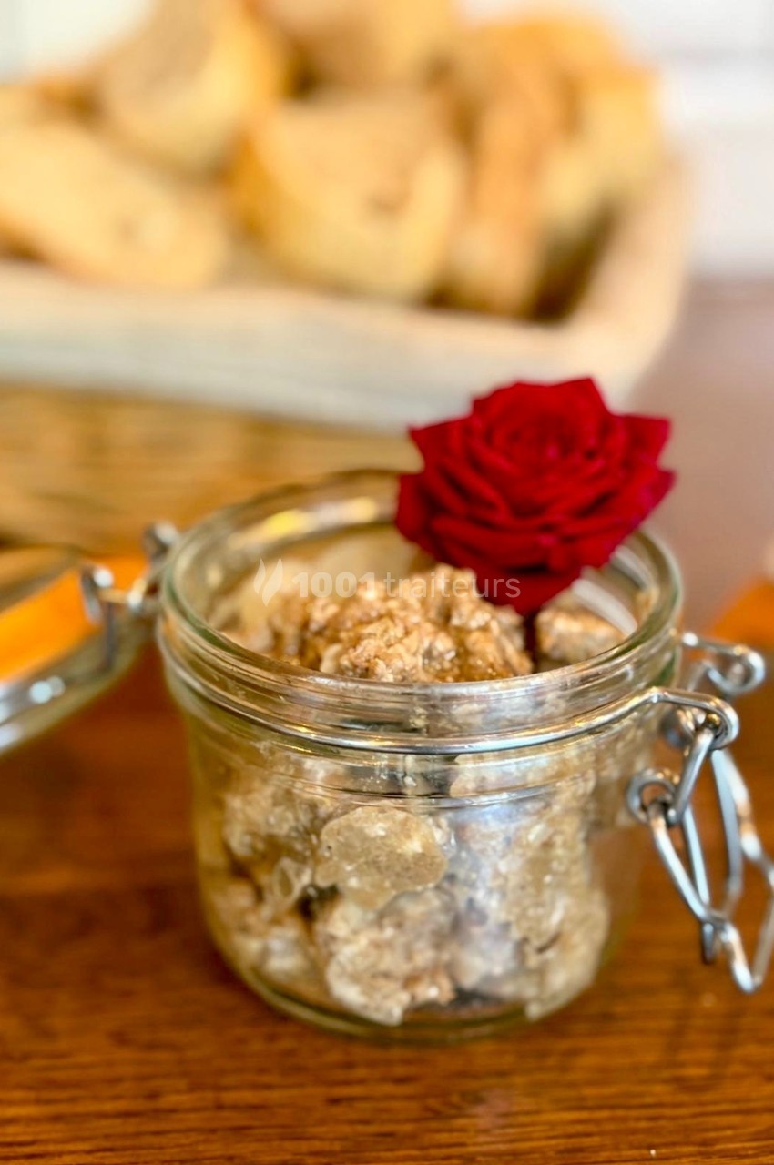 Bocal en verre ouvert contenant des morceaux de truffes, décoré d'une rose rouge, avec des tranches de pain en arrière-plan.
