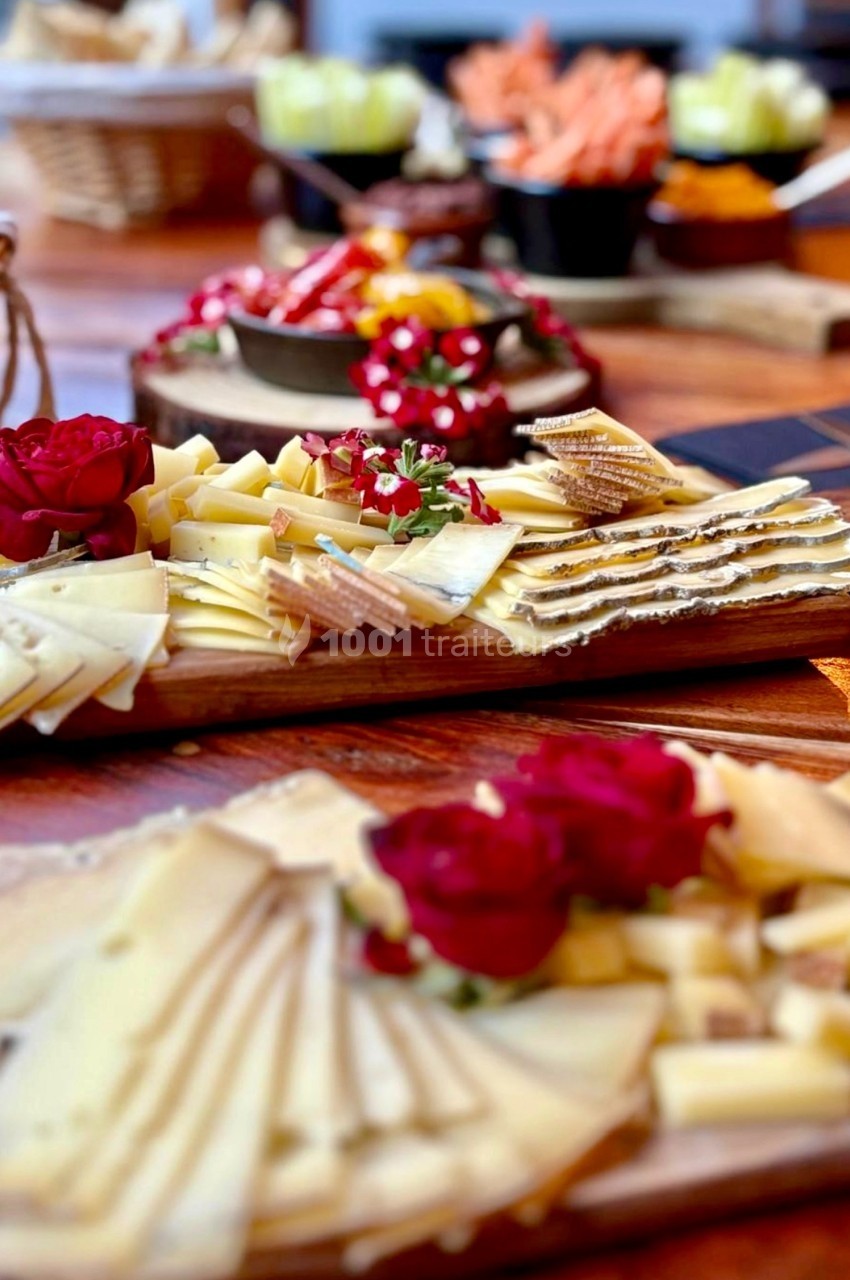 Plateaux de fromages variés avec décorations florales rouges, disposés sur une table en bois.