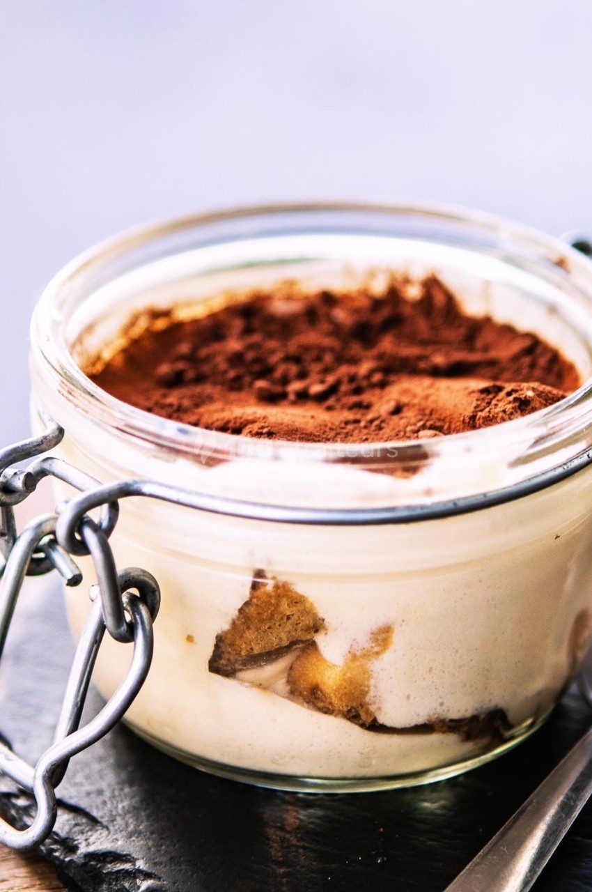 Dessert tiramisu dans un bocal en verre, avec une couche de cacao en poudre sur le dessus.