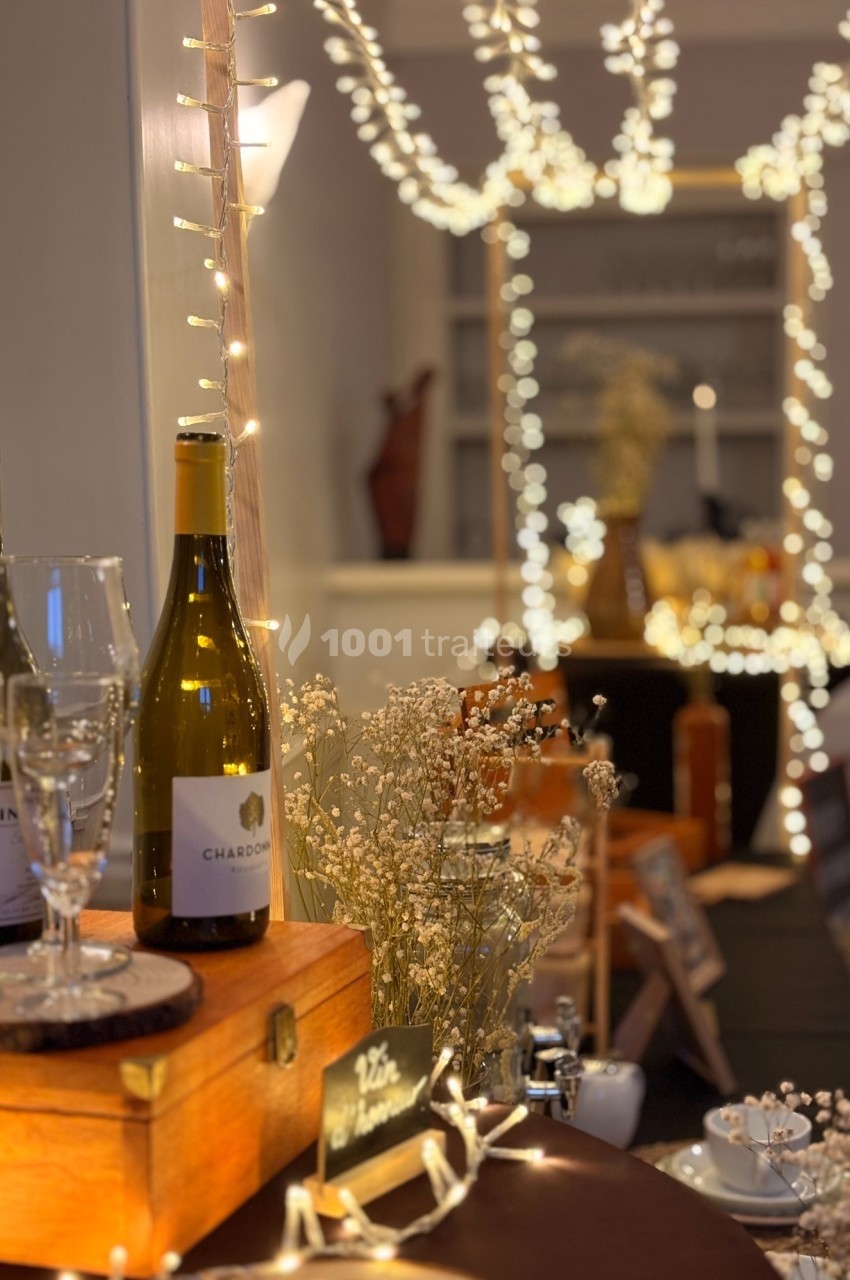 Bouteille de vin blanc, verres et décorations lumineuses sur une table en bois dans une ambiance chaleureuse.