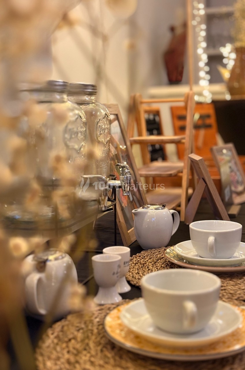 Table dressée avec tasses blanches, théières et distributeurs de boissons, décorée dans un style chaleureux et rustique.