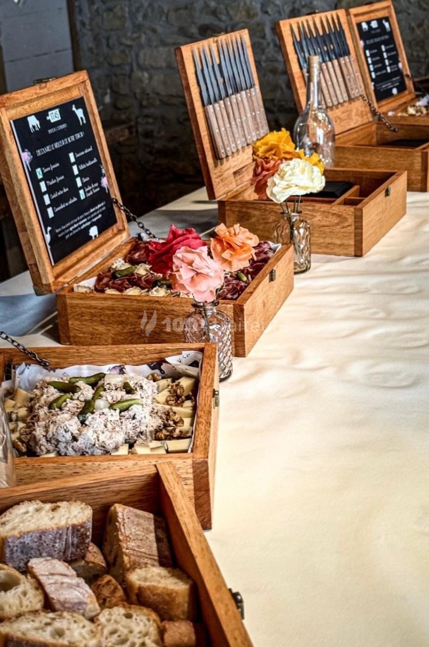Plateau de dégustation avec pains, fromages, charcuteries et fleurs décoratives, présenté dans des boîtes en bois.