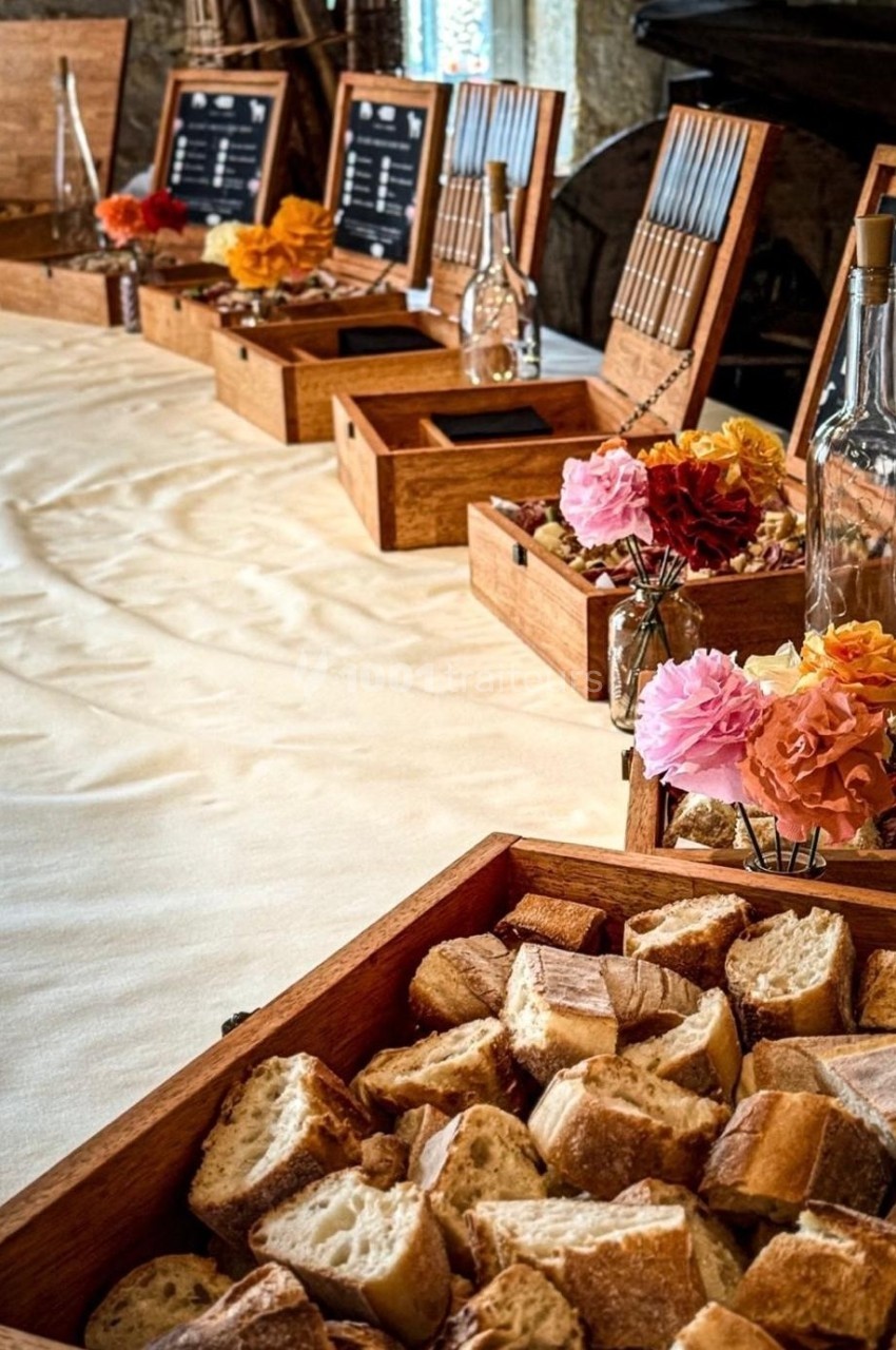 Plateau de morceaux de pain devant une table décorée de fleurs, avec des boîtes en bois et des menus en arrière-plan.