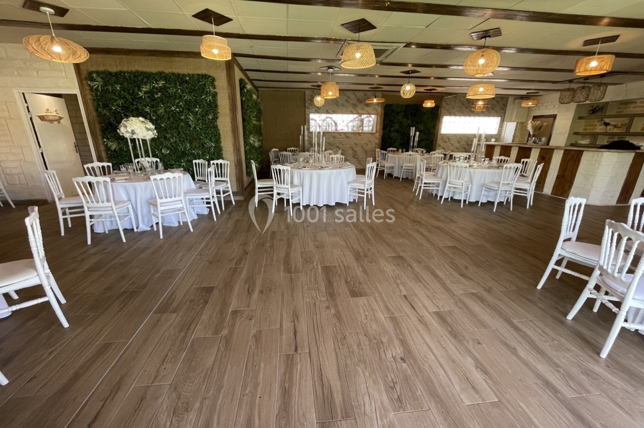 Salle de réception décorée avec des tables rondes dressées, des chaises blanches et des murs végétalisés.