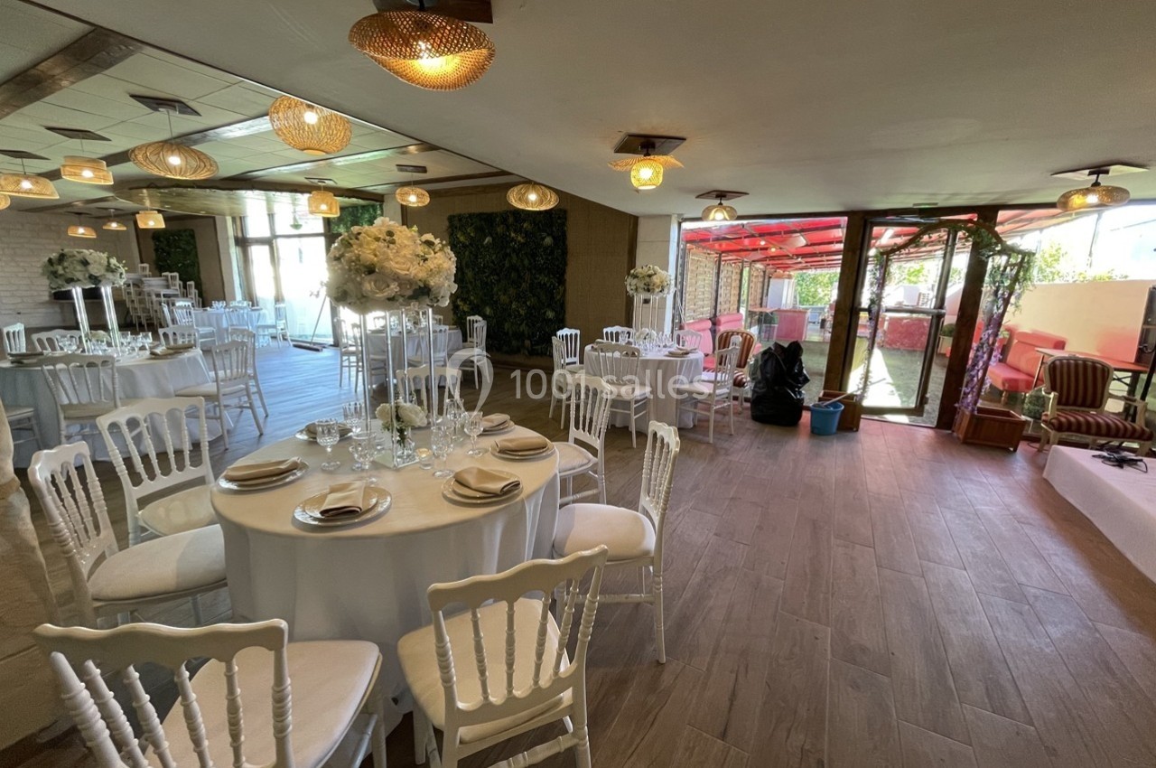 Salle de réception décorée avec des tables rondes, nappes blanches, chaises élégantes et compositions florales.