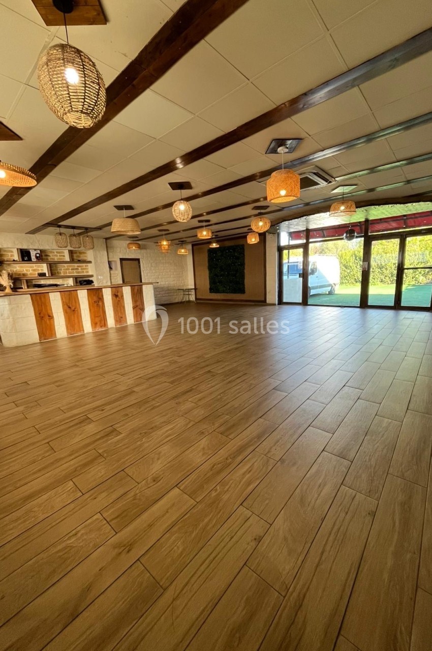 Salle lumineuse avec parquet en bois, comptoir en pierre et bois, grandes fenêtres donnant sur un espace extérieur verdoyant.