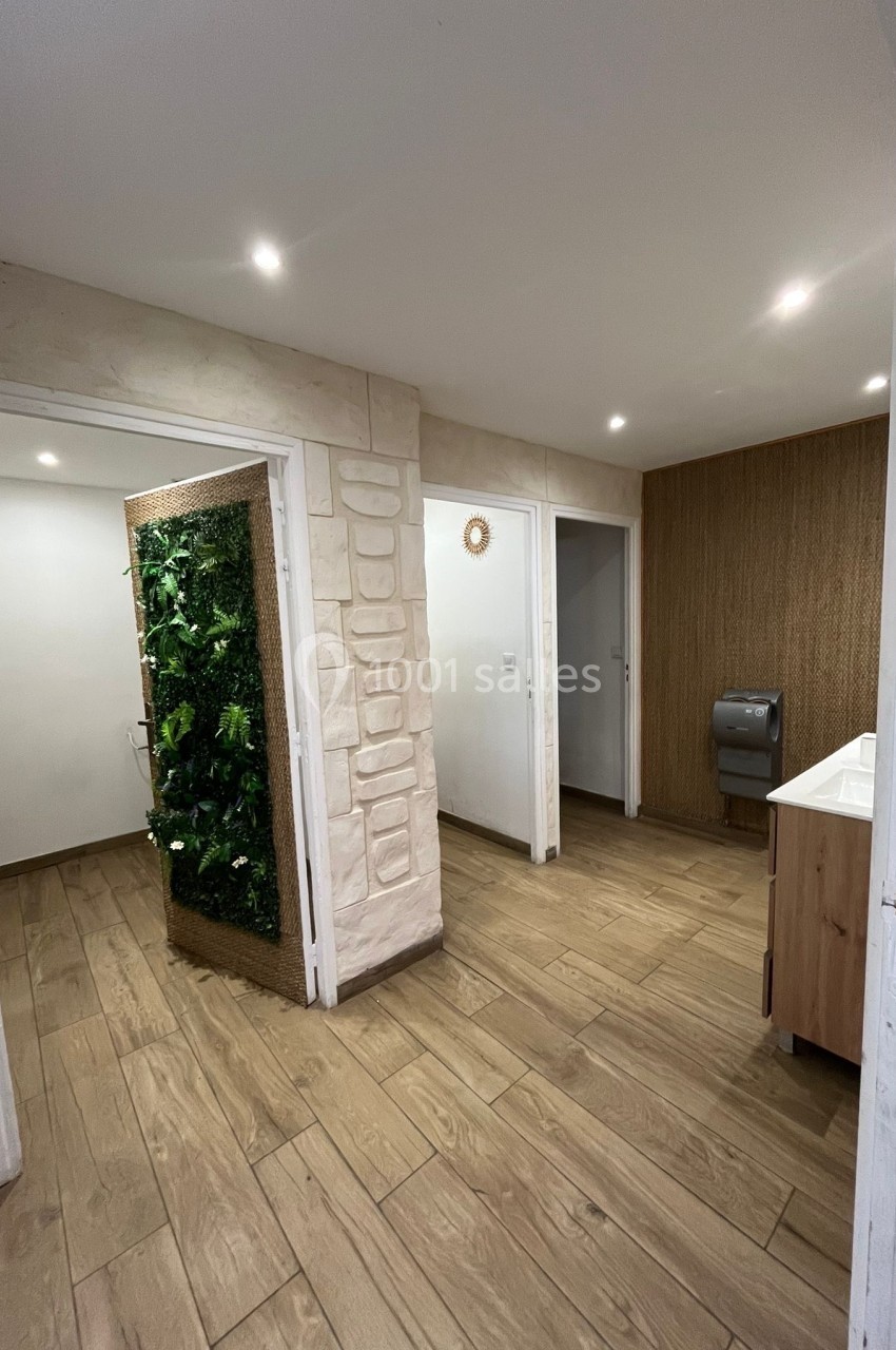 Vue d'un espace intérieur avec sol en bois, mur végétal, lavabo, distributeur de papier et éclairage encastré.