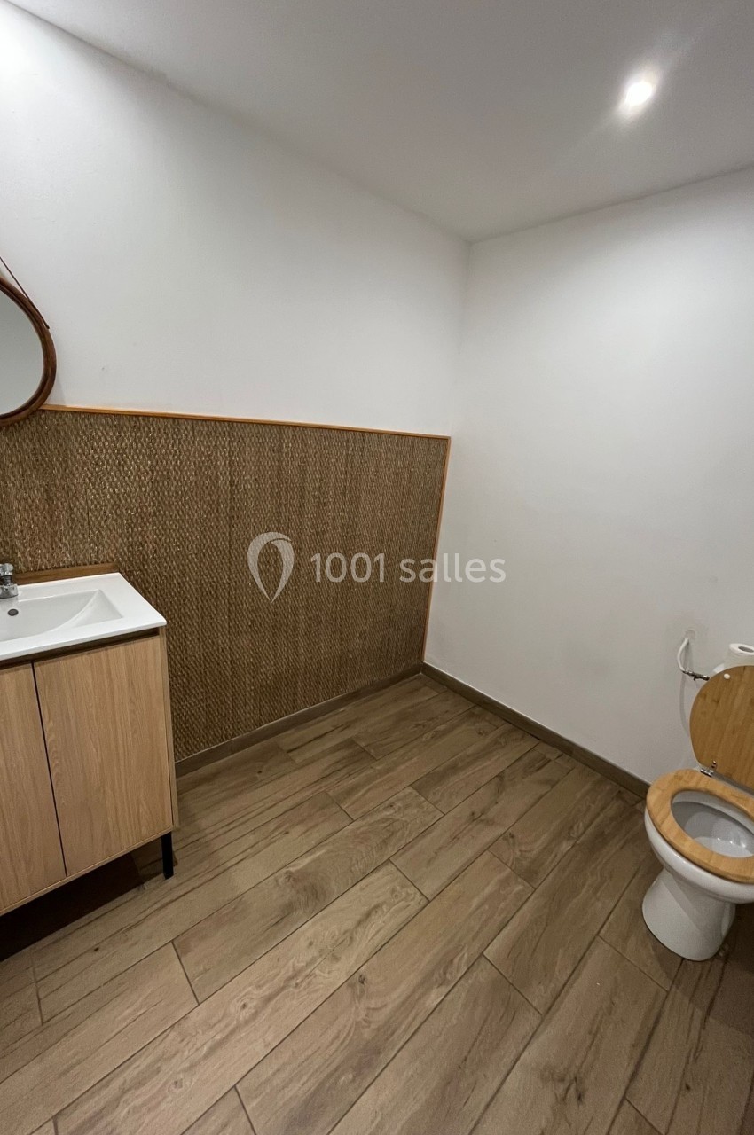Salle de bain avec sol en bois, lavabo sur meuble en bois clair, miroir rond et toilettes avec abattant en bois.