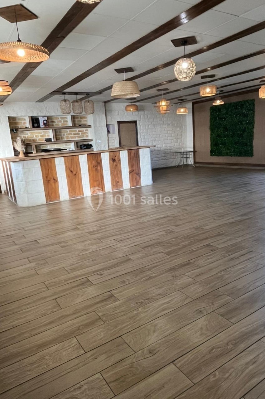Salle lumineuse avec parquet en bois, comptoir en bois et pierre, suspensions en osier et mur végétal en arrière-plan.