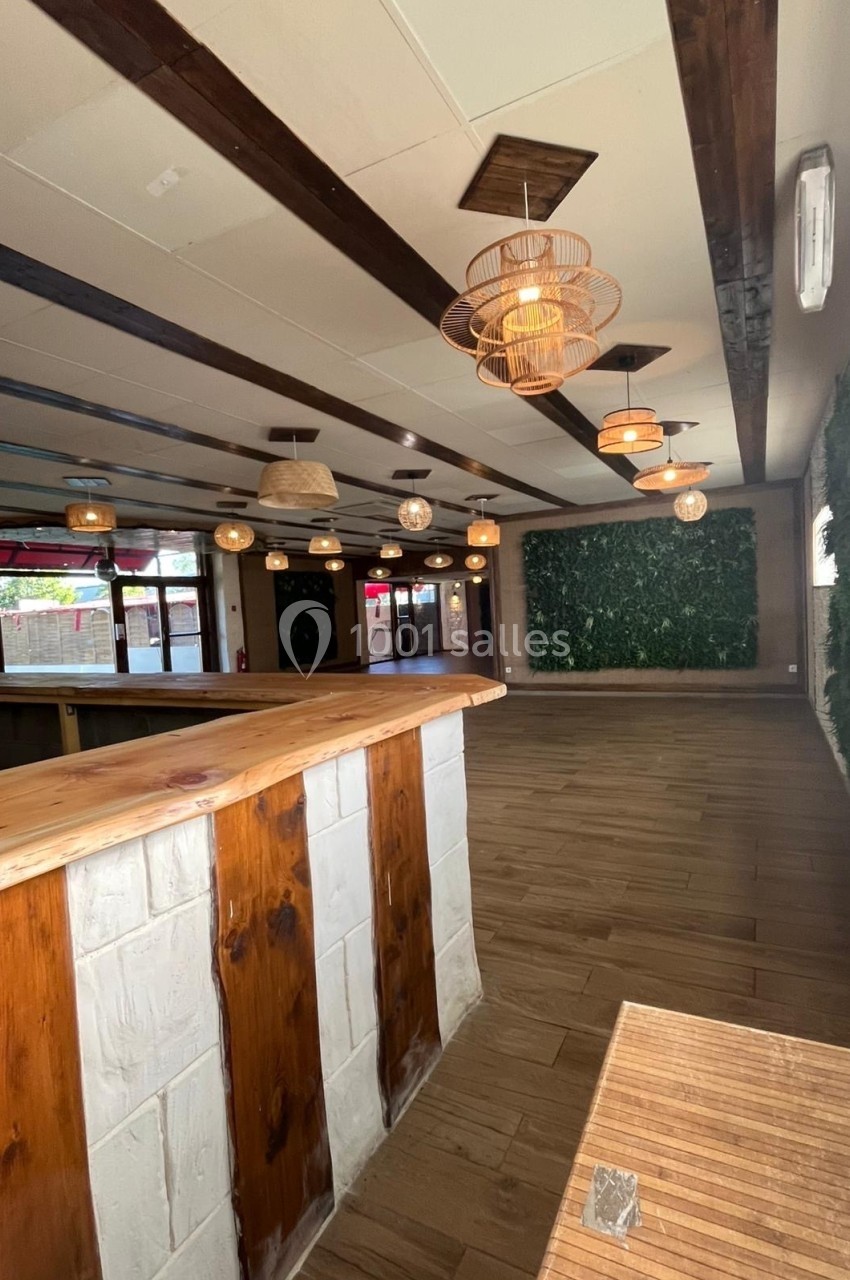 Intérieur d'un espace avec comptoir en bois, murs végétalisés, luminaires suspendus et sol en parquet.