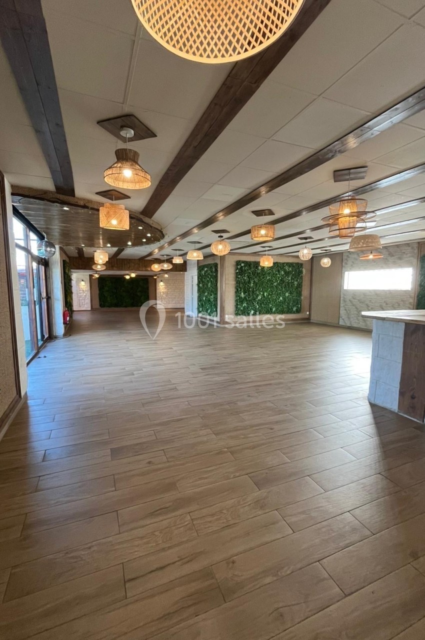 Salle spacieuse avec parquet en bois, murs végétalisés et plafonds ornés de luminaires suspendus.