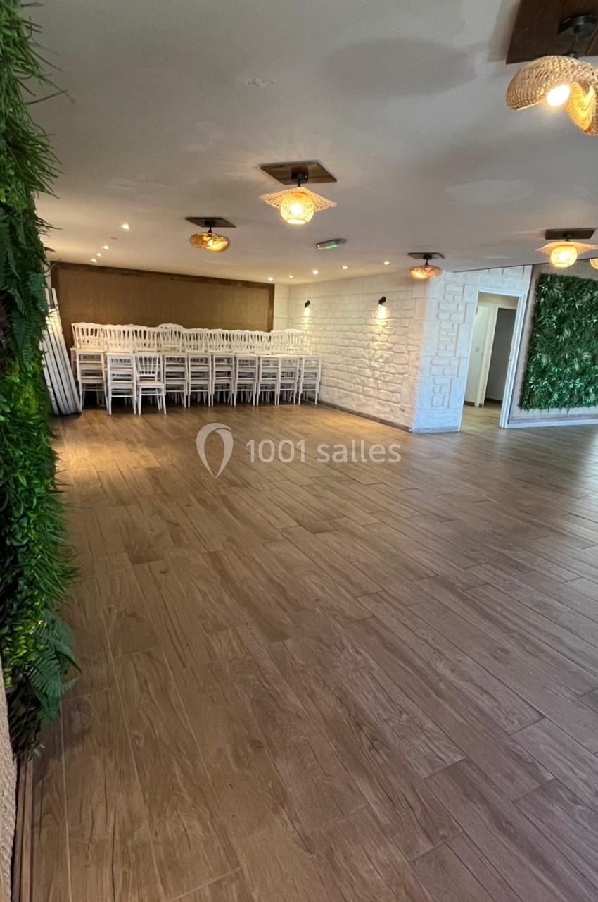 Salle lumineuse avec parquet en bois, murs décorés de végétation et chaises blanches empilées dans un coin.