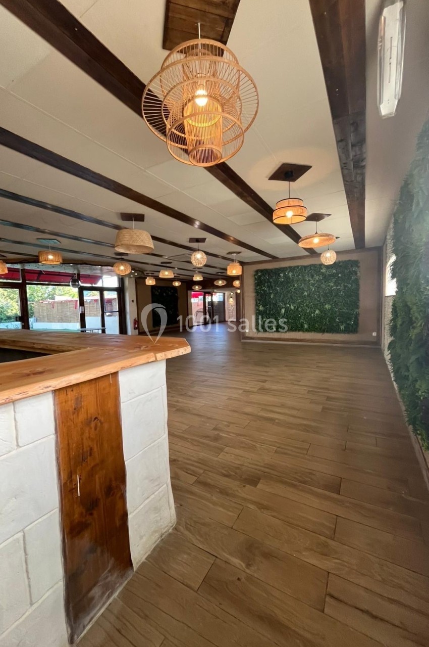 Salle lumineuse avec parquet en bois, murs végétalisés, plafonniers suspendus et grandes baies vitrées.
