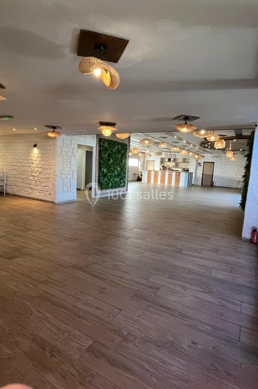 Salle spacieuse avec parquet, murs en pierre, éclairage suspendu et un bar au fond.