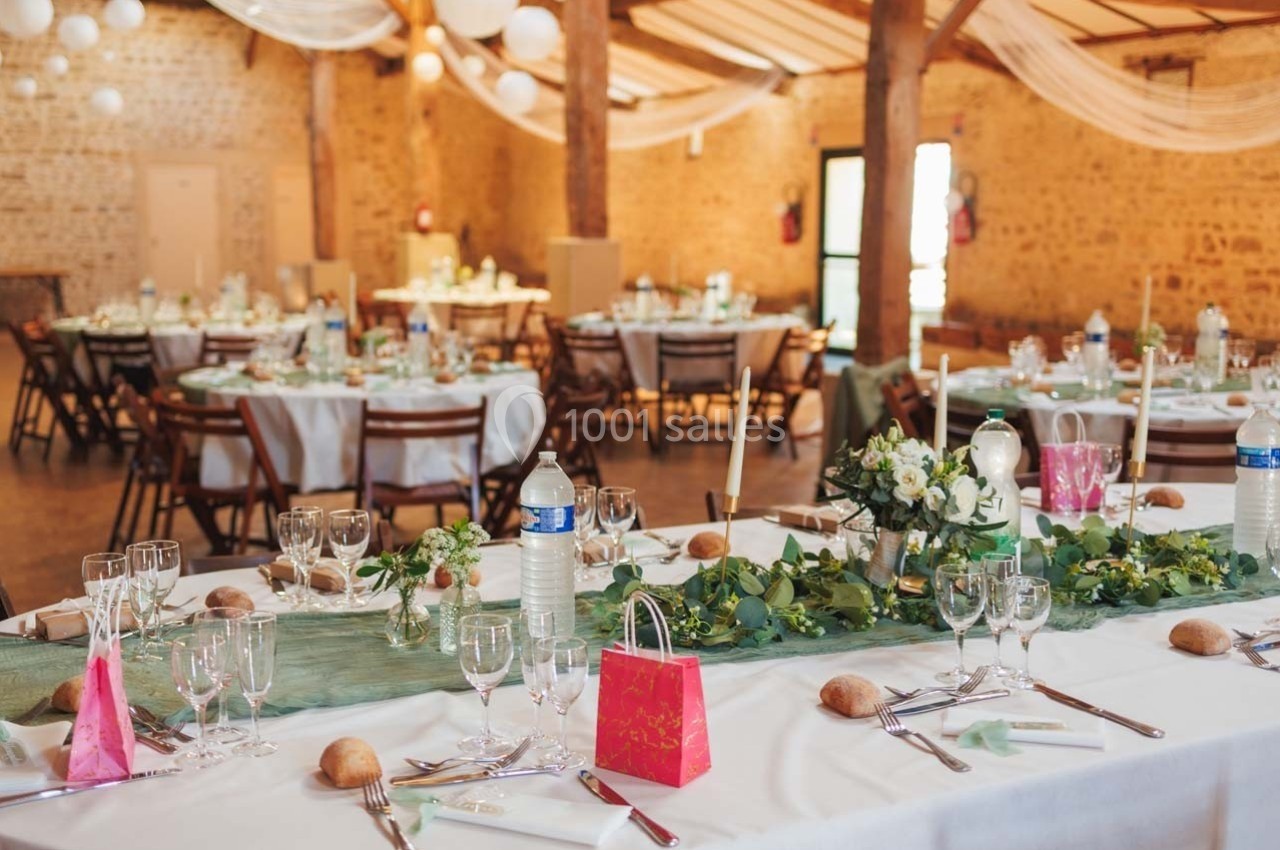 Salle de réception décorée pour un mariage avec tables dressées, nappes blanches, bouquets et éléments de décoration verts.