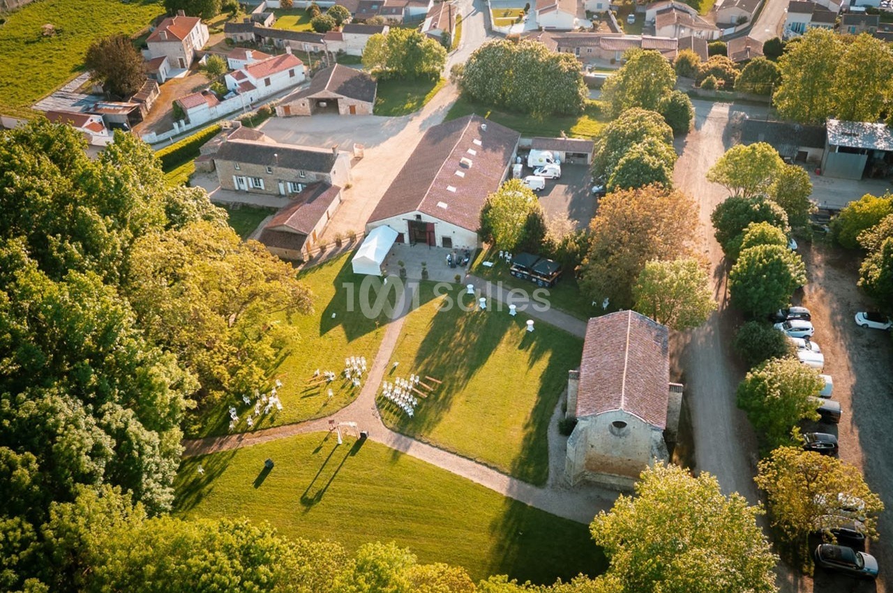 Vue aérienne d'un domaine rural avec bâtiments, espaces verts et installation de chaises en extérieur.