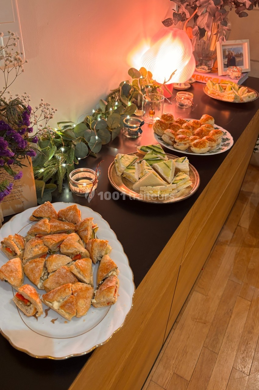 Assortiment de plats salés disposés sur un buffet en bois, décoré de guirlandes lumineuses et de fleurs.