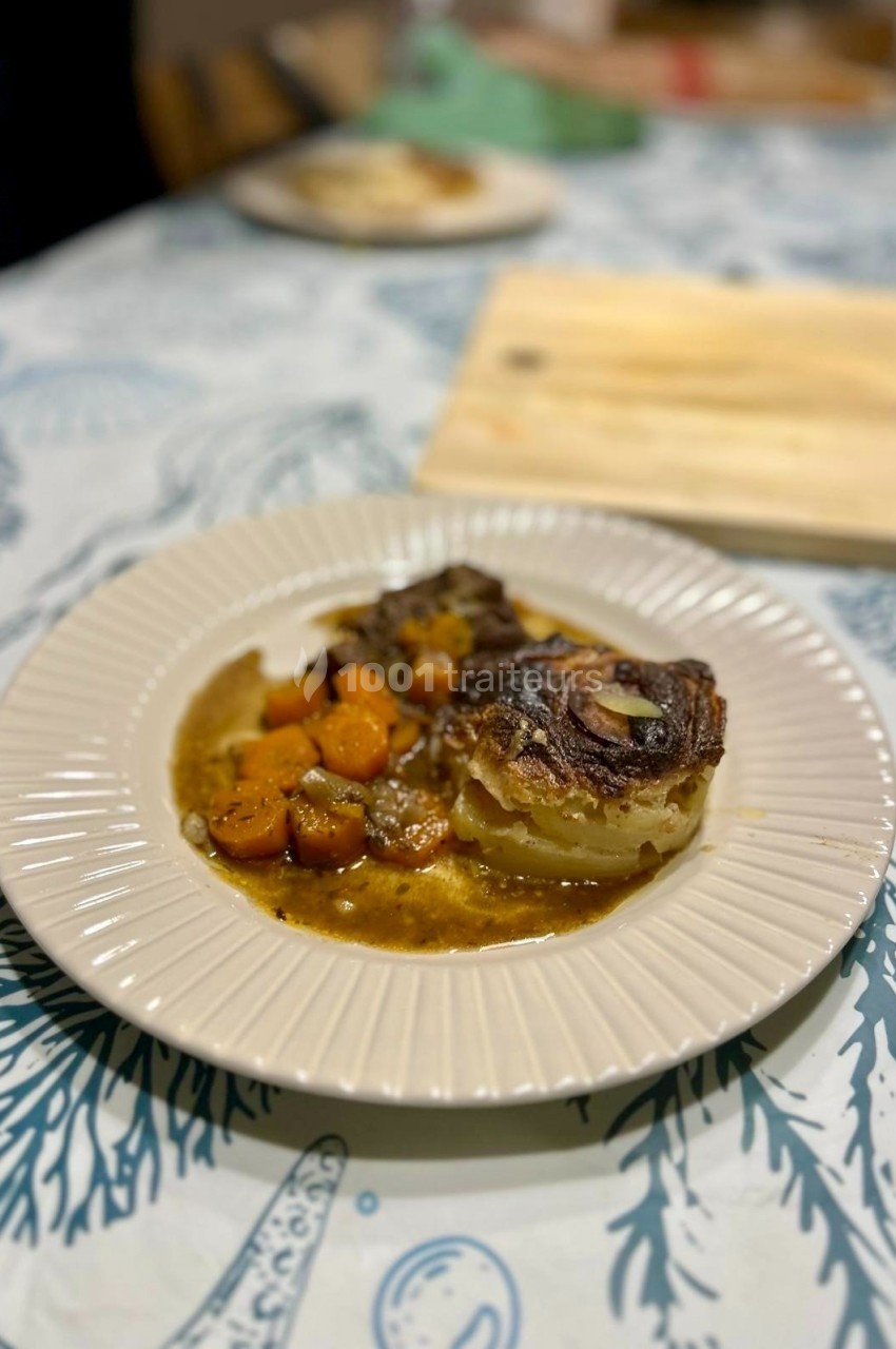 Assiette contenant un gratin de pommes de terre accompagné de carottes et d'une sauce, posée sur une nappe à motifs marins.