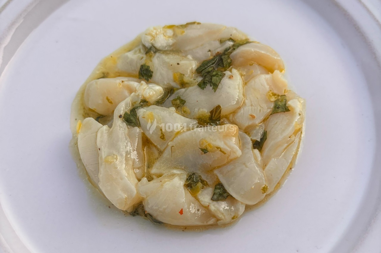 Tranches de noix de Saint-Jacques marinées à l'huile et aux herbes, présentées sur une assiette blanche.