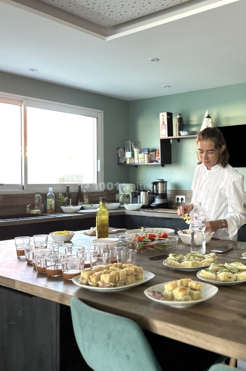 Une femme prépare des plats sur un grand plan de travail dans une cuisine lumineuse et moderne.