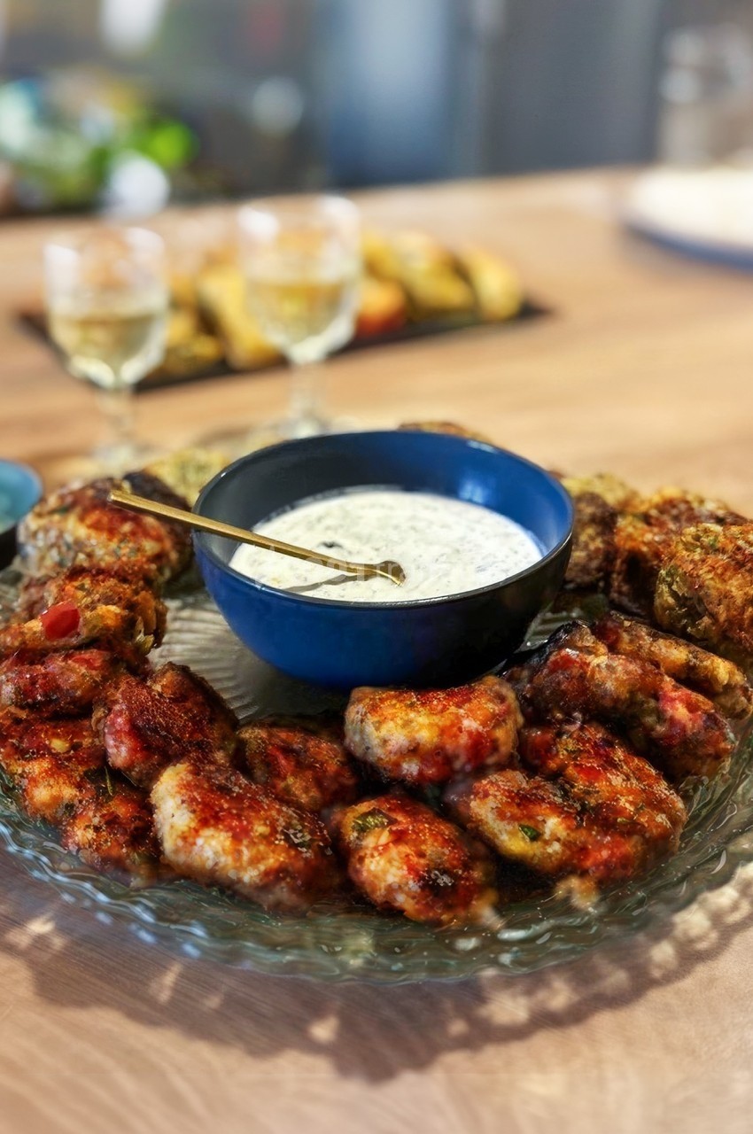 Assiette de boulettes de viande grillées entourant un bol de sauce blanche sur une table en bois.