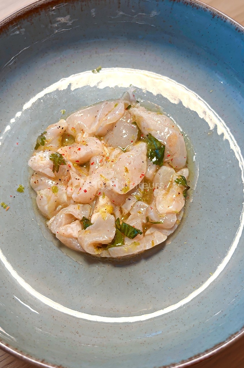 Assiette contenant un tartare de poisson cru assaisonné, servi dans un bol bleu sur une table en bois.
