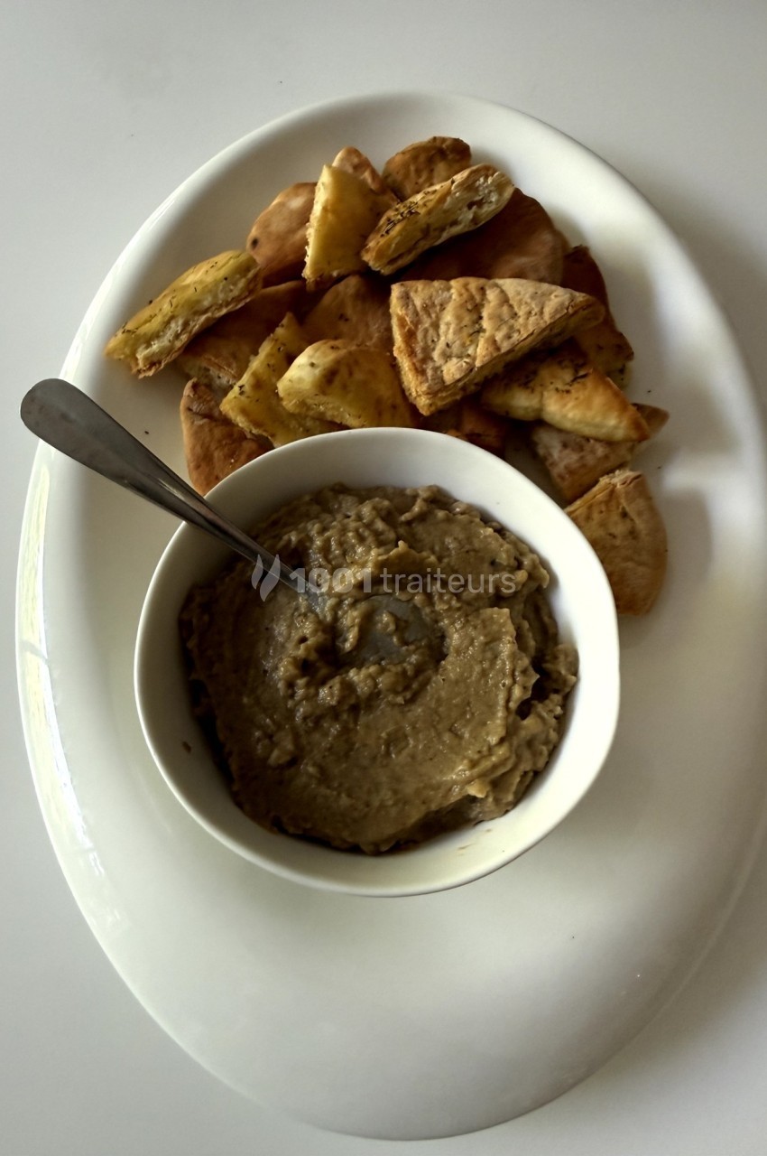 Bol de houmous accompagné de morceaux de pain pita grillés disposés sur une assiette blanche.
