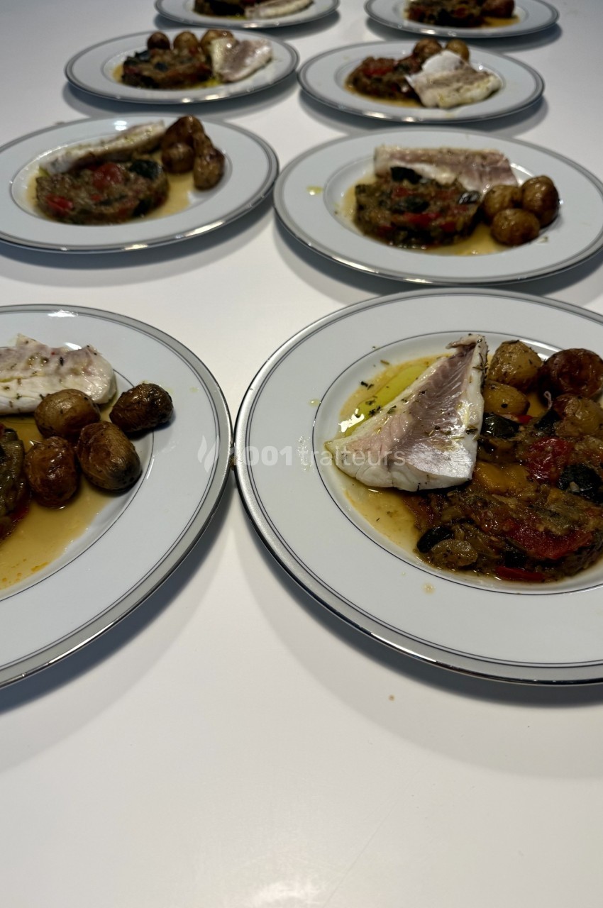 Assiettes garnies de poisson, légumes grillés et pommes de terre rôties, disposées sur une table blanche.