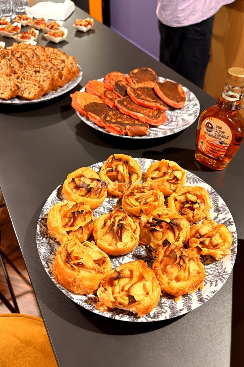 Assortiment de viennoiseries, pancakes et biscuits présentés sur une table noire avec une bouteille de sirop d'érable.