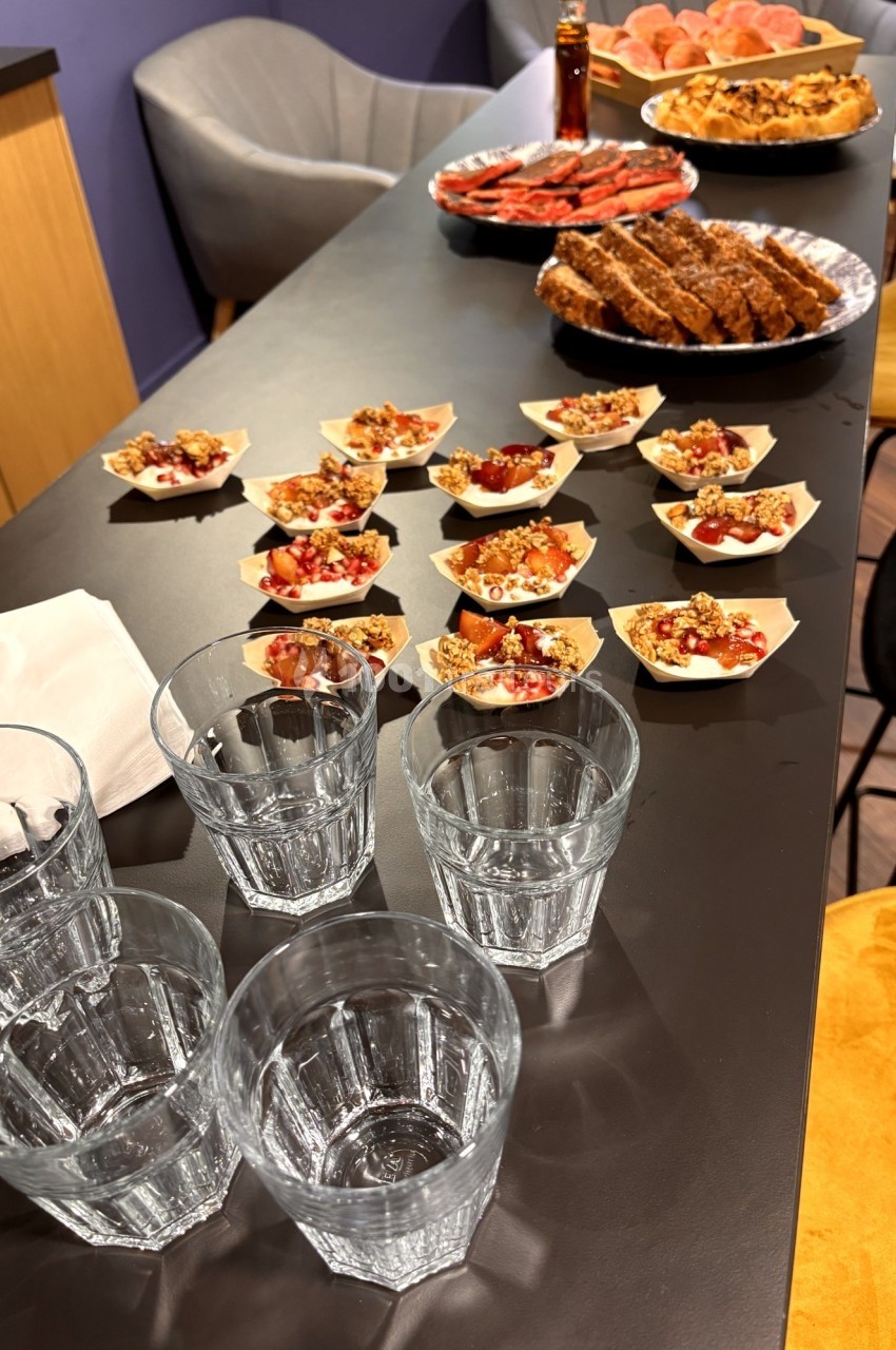 Table avec des verrines de fruits, des plats de pâtisseries et des verres en verre, dans un cadre intérieur.
