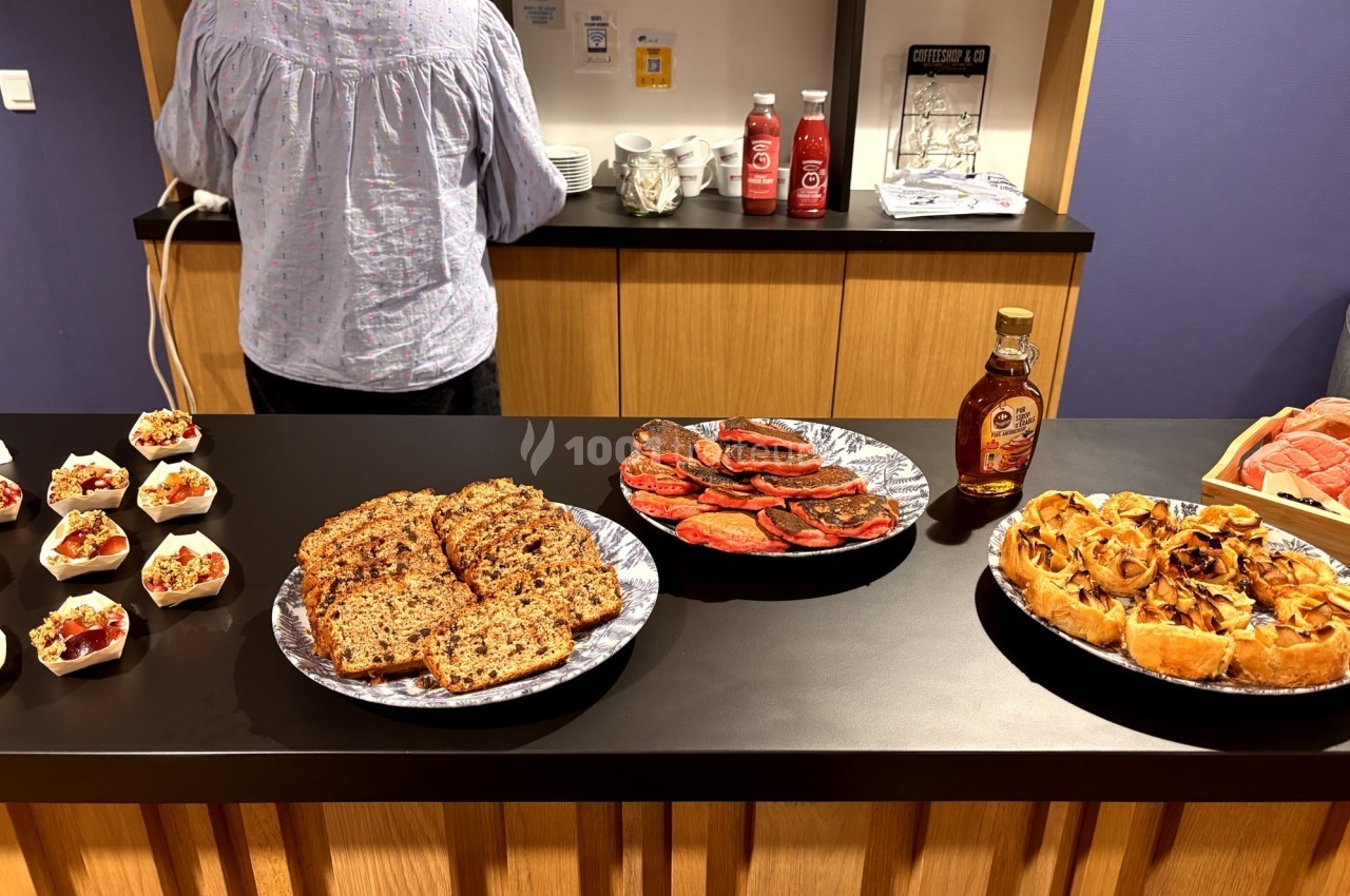 Buffet avec des plats variés : pain aux graines, charcuterie, tarte salée et verrines, sur un comptoir en bois.