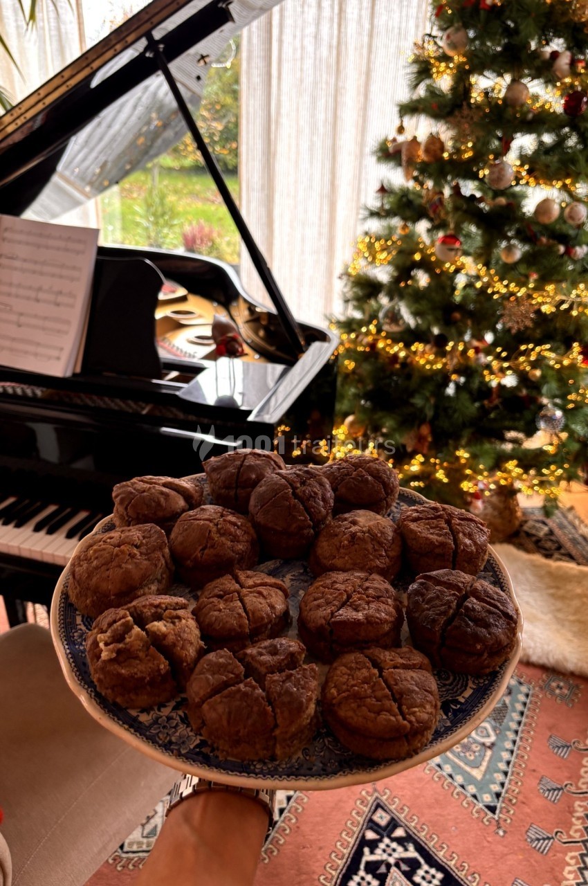 Assiette de muffins au chocolat tenue devant un piano à queue et un sapin de Noël décoré.