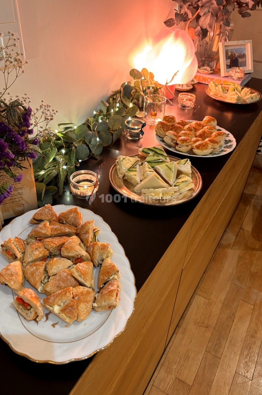 Plats variés de sandwichs et amuse-bouches disposés sur un buffet décoré de guirlandes lumineuses et de fleurs.