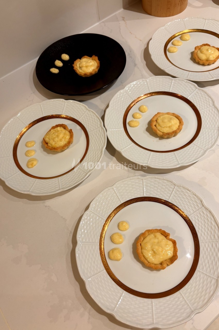 Assiettes contenant des tartelettes garnies de crème, accompagnées de points de sauce, disposées sur une table.
