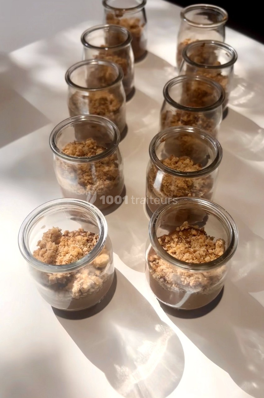 Desserts individuels en verrines contenant une base crémeuse surmontée de crumble, disposés sur une table blanche.
