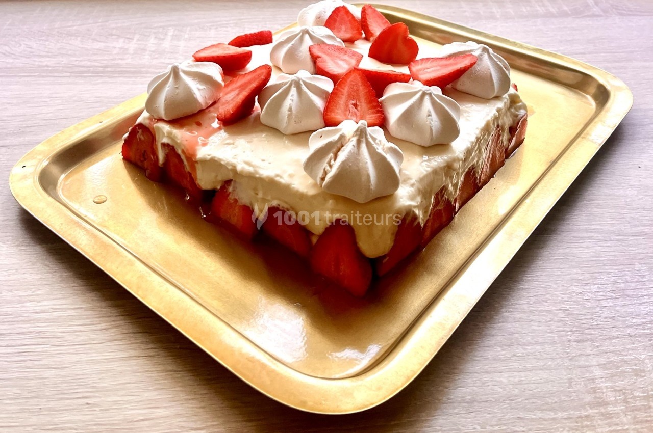 Gâteau décoré de fraises fraîches et de meringues blanches, présenté sur un plateau doré.