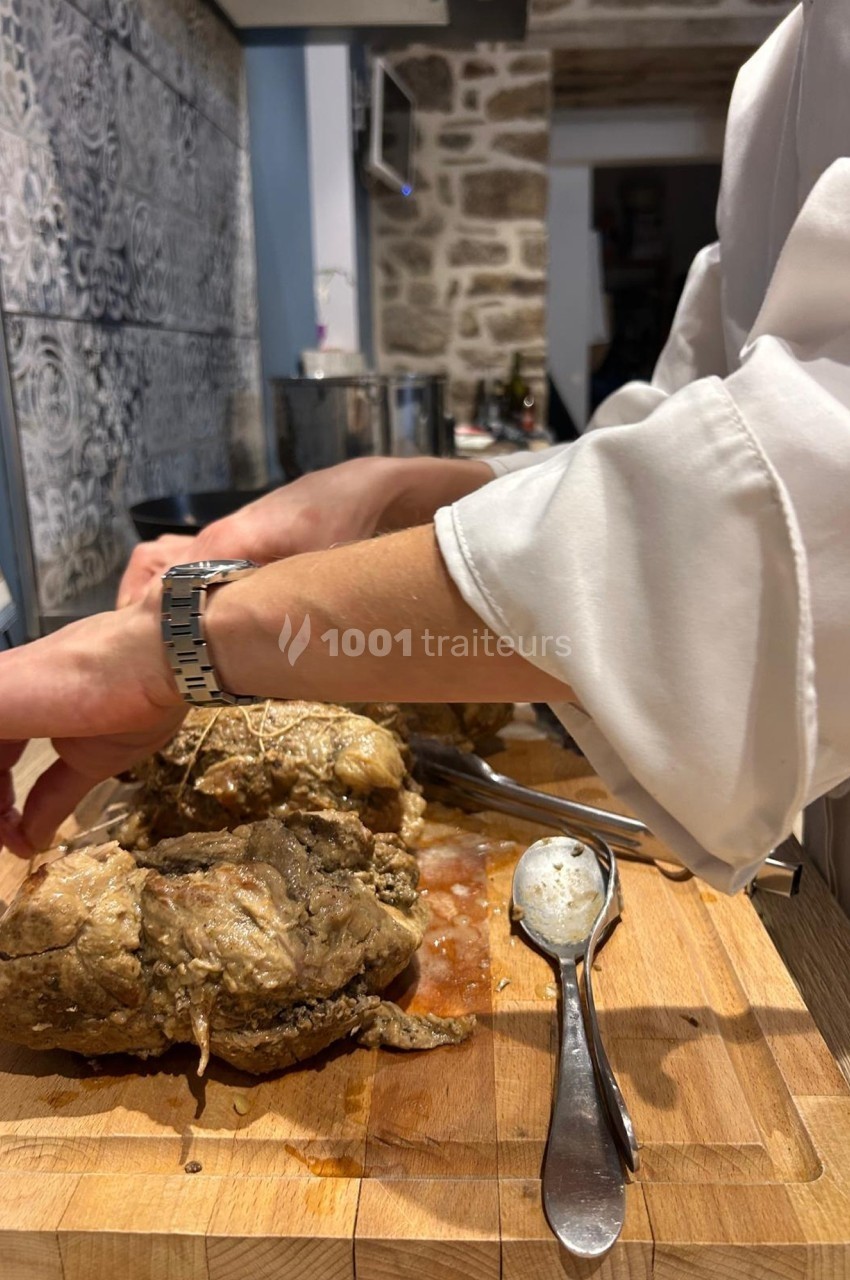 Un cuisinier attache une pièce de viande cuite sur une planche en bois, entourée d'ustensiles de cuisine.