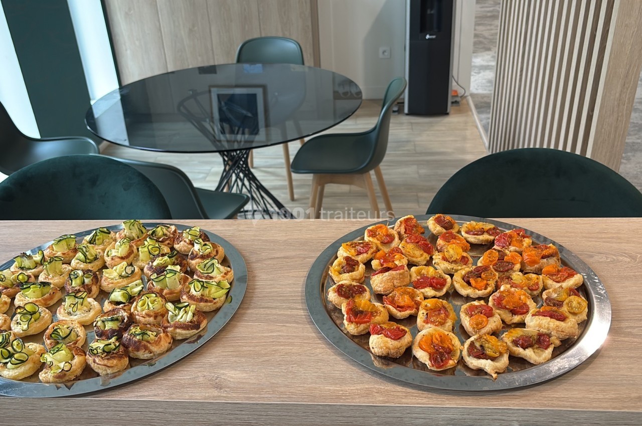 Plateaux de bouchées apéritives variées disposés sur un comptoir en bois dans un espace moderne avec table et chaises.