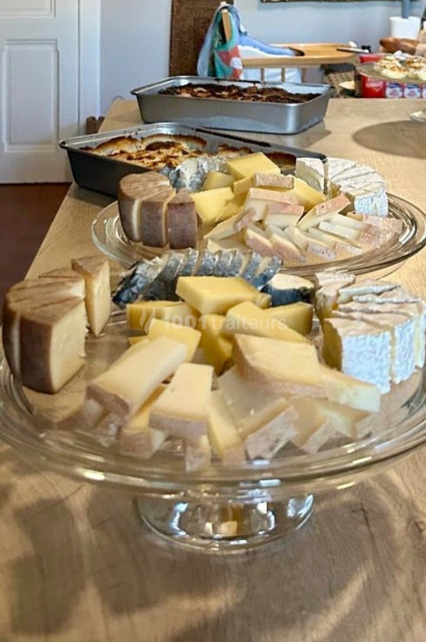 Plateaux de fromages variés disposés sur des supports en verre, avec des plats en arrière-plan sur une table en bois.